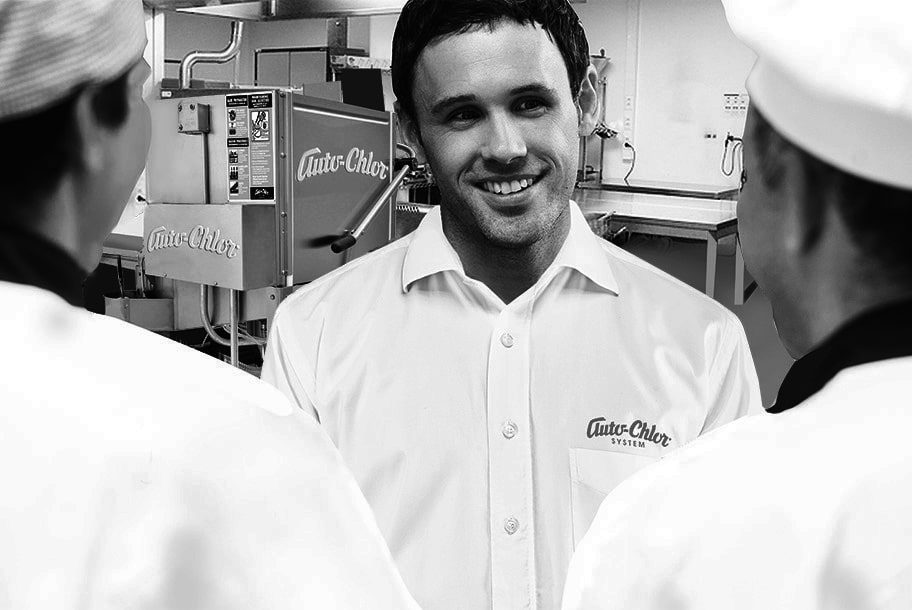 Smiling man in an Auto-Chlor uniform with dishwashing equipment in the background.